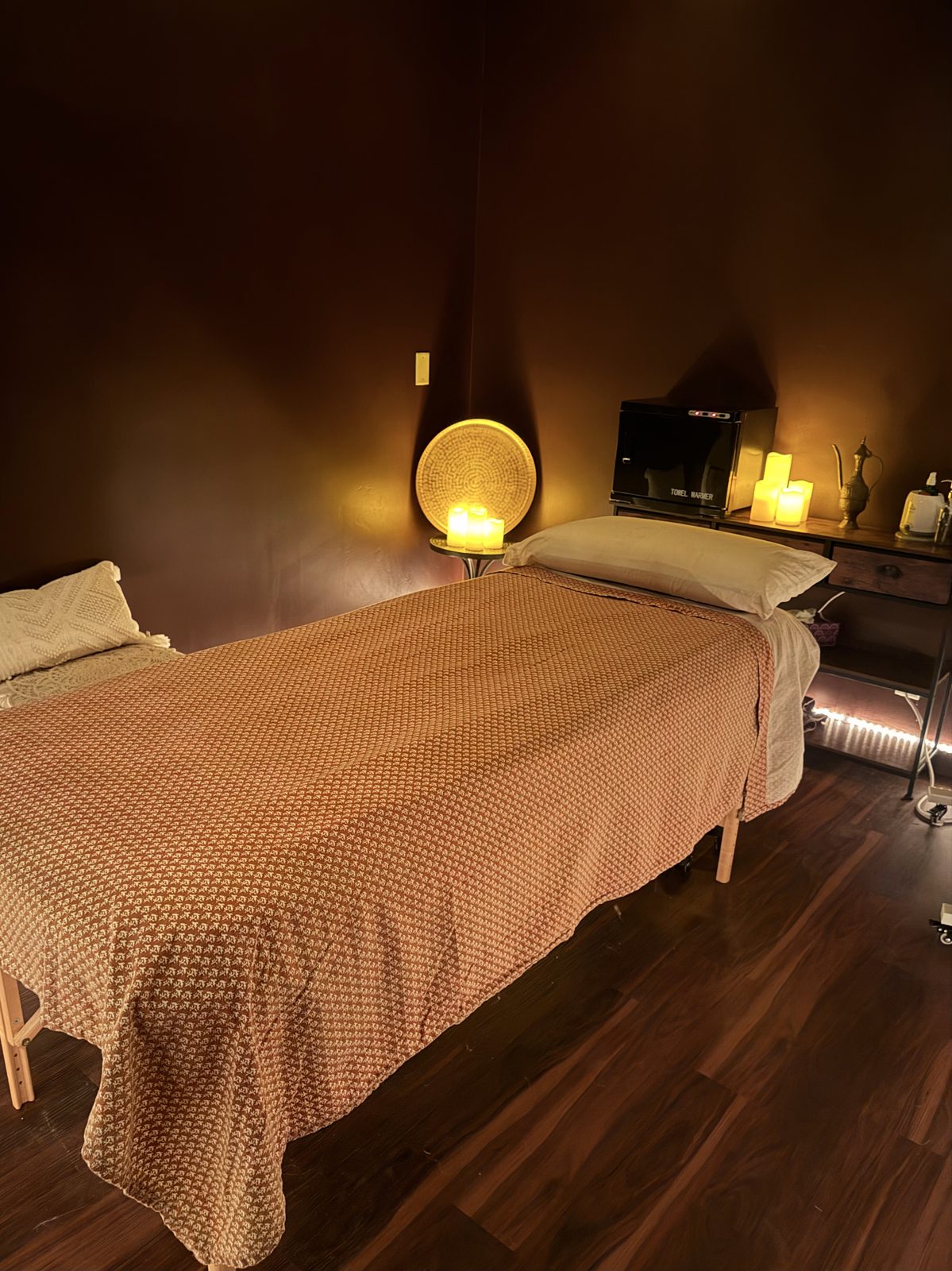 A bodywork room at Barefoot Sage Center — a massage table dressed in a textured throw, warm sconce light, candles, and a small altar of brass and woven elements